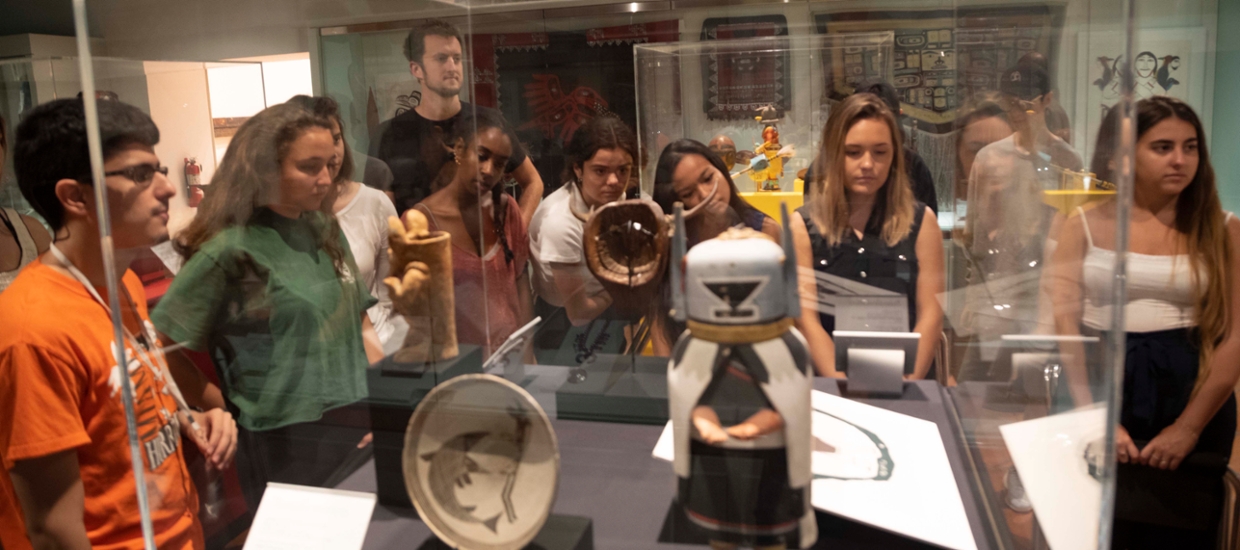 students looking at a case of native american art consisting of small wooden carved sculptures and ceramic pots