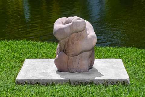 stone sculpture of humanoid form seated and holding themself wrapped within their arms creating almost a ball shape