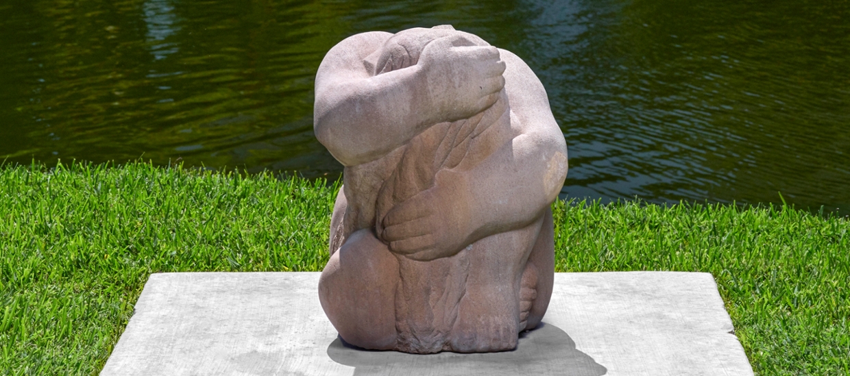 stone sculpture of humanoid form seated and holding themself wrapped within their arms creating almost a ball shape