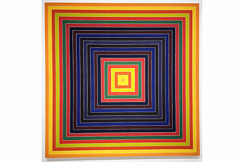 This 11 foot by 11 foot square acrylic painting features a series of concentric squares in oranges, reds, greens, and blues, with a small orange square at its center. The square bands of color resemble thin frames nestled one inside the other, receding toward the small orange square at the center. The precisely aligned corners of the squares, the arrangement of colors (warm colors at the edges, dark near the middle, and bright at the center), and the small square at the core, combine to create  a tunnel effect or illusion. 