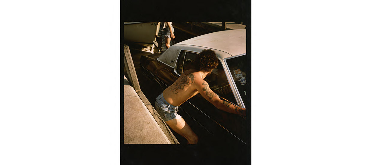 photograph of a man shirtless from the back leaning into a car