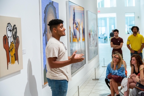 student talking to seated students in the middle of an art gallery