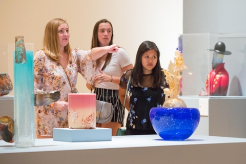 three woman looking at glass art in an art gallery. Glass objects are vase like