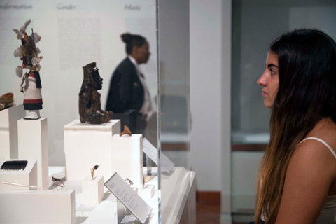 image of a woman looking into a glass case with native american art depicting small figures made of wood and cloth