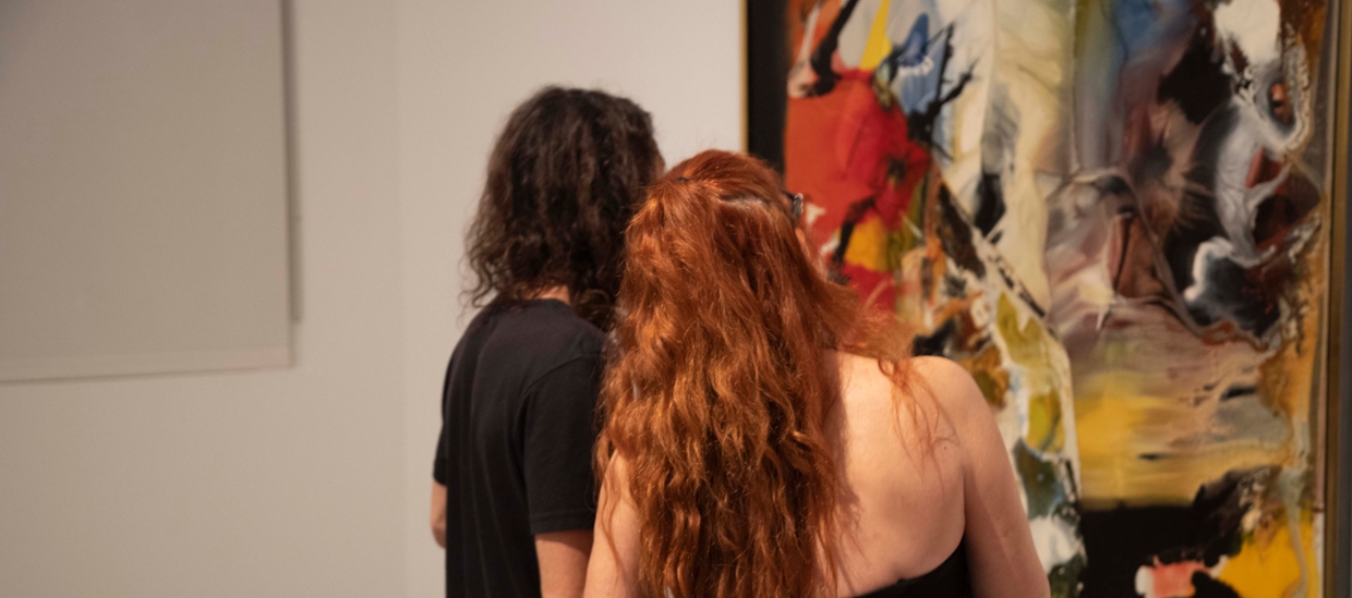 two people being seen from behing looking at an abastract work of art in many colors