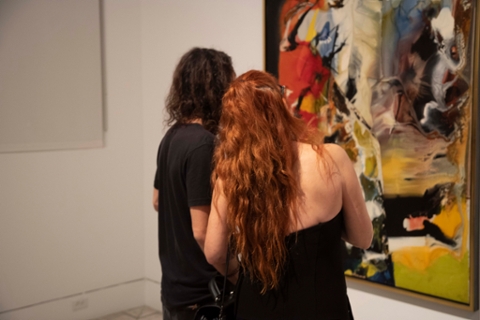 two people being seen from behing looking at an abastract work of art in many colors