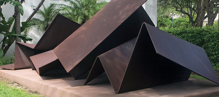 image of a contemporary abstract outdoor sculpture made of metal that is in folded geometric shapes. Metal is rust colored