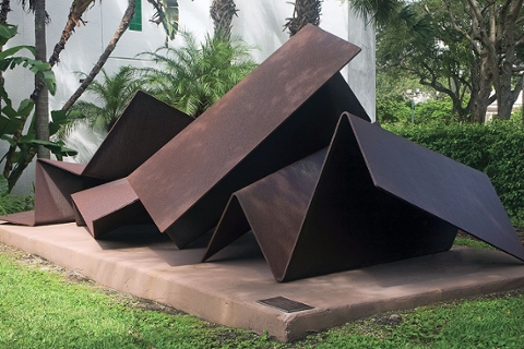 image of a contemporary abstract outdoor sculpture made of metal that is in folded geometric shapes. Metal is rust colored