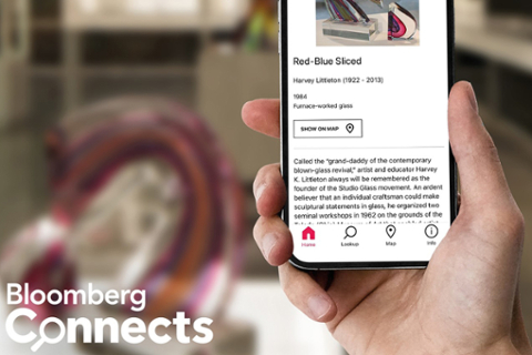 image of a hand holding a mobile phone with an app open. The text stating "Bloomberg Connects" is in the left corner of the image. 