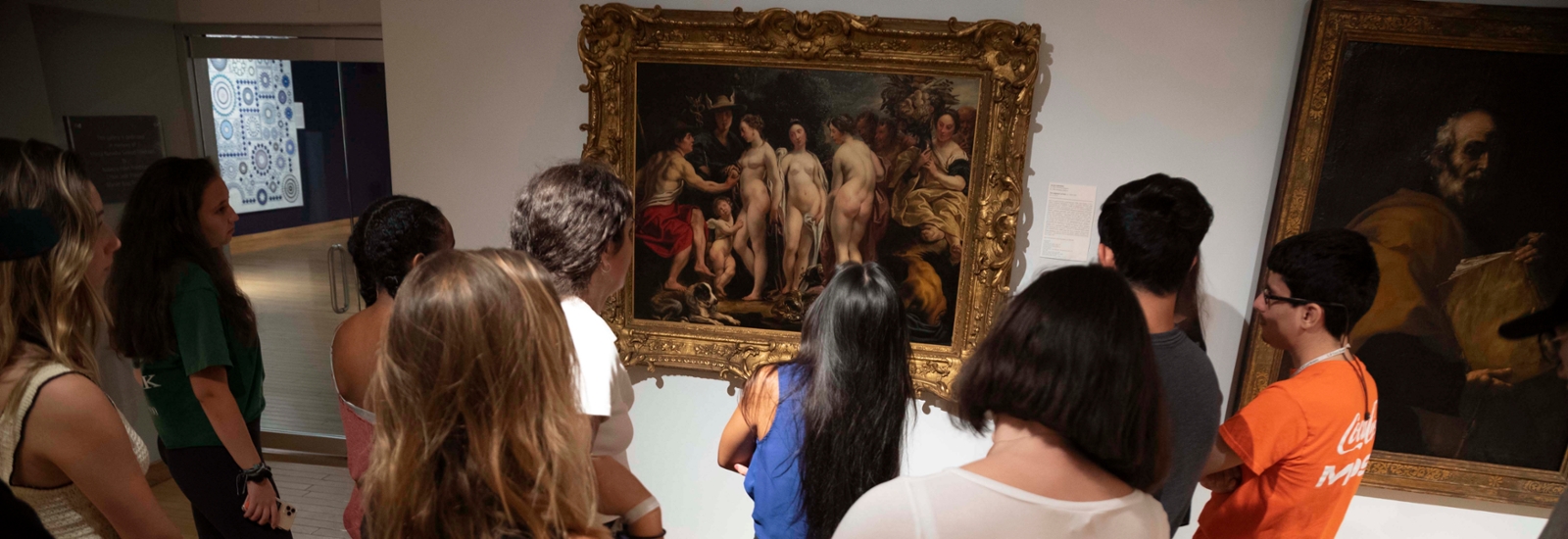 image of a group of students with their back to the viewer are looking at a painting done in classical style depicting the judgement of paris