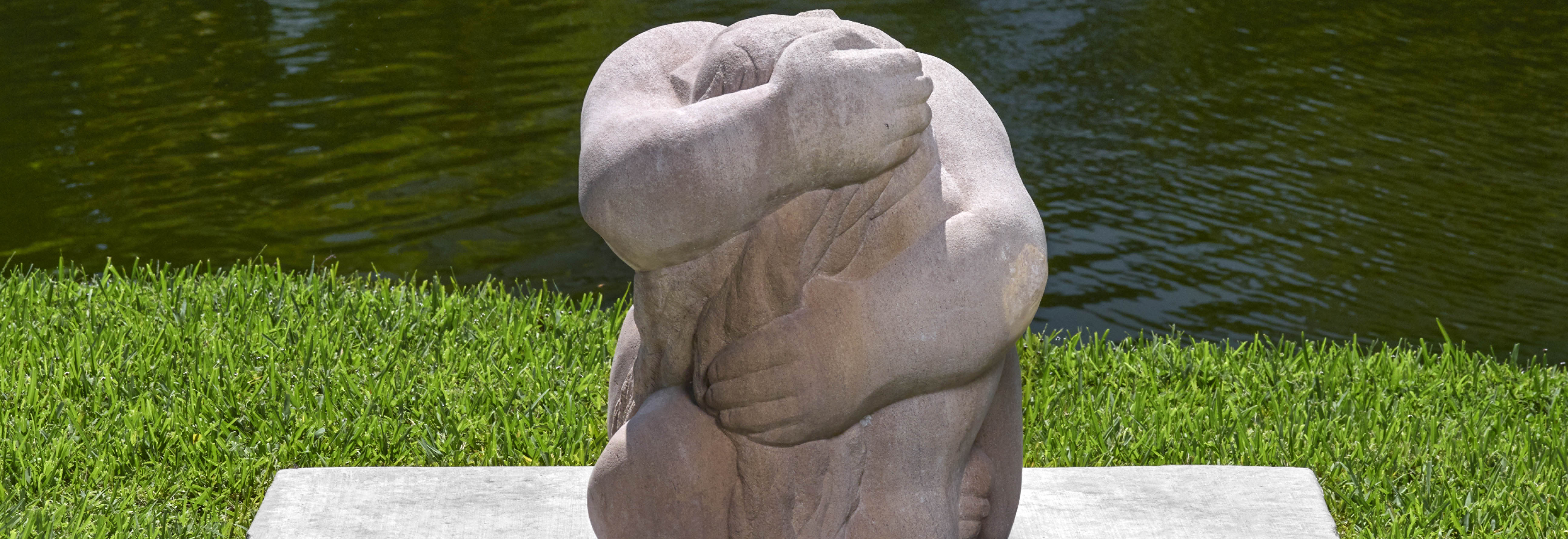 stone outdoor sculpture of a seated figure holding themselves in their arms forming almost a spherical shape with their entire body