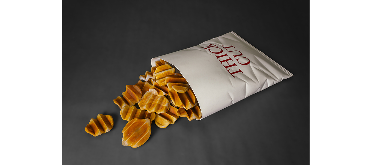 glass sculpture of realistic looking thick cut french fries in a glass bag laying on the ground with fries spilling out. The glass bag has the words thick cut on it. 