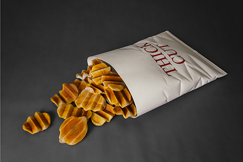glass sculpture of realistic looking thick cut french fries in a glass bag laying on the ground with fries spilling out. The glass bag has the words thick cut on it. 