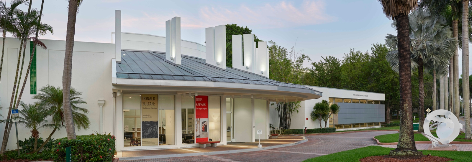 exterior image of the Lowe Art Museum showing the front entrance in the foreground and the palley pavillion in the backgroud with palm trees in the middle ground