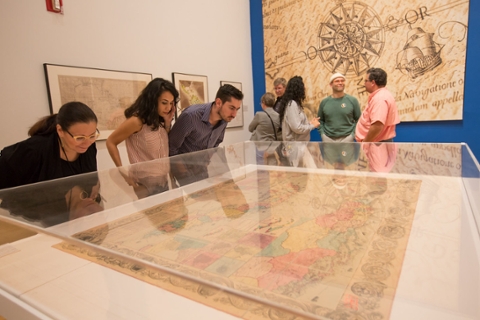 image of college students and members looking at cases with maps in them within museum gallery