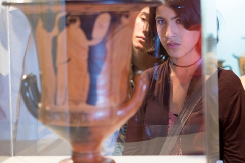 image of a woman looking at an ancint Greek vase that is red and black 