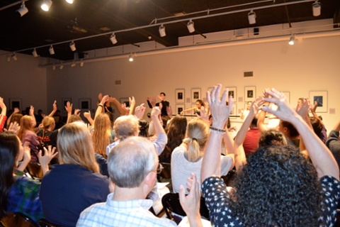 image of adults in gallery all raising hands as they participate in a program