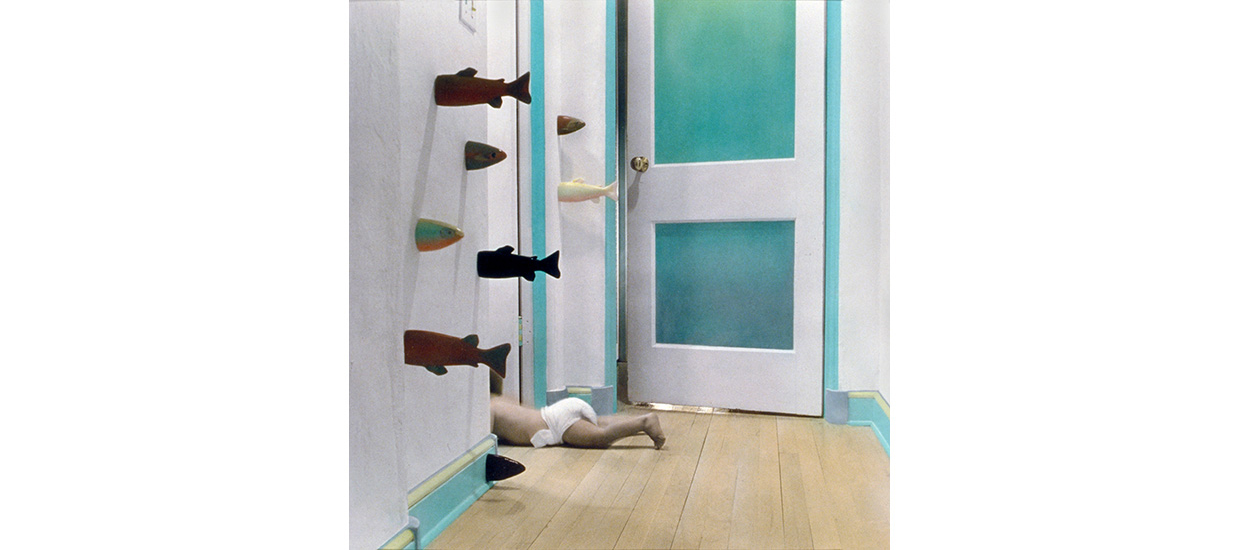 image of a room with a baby doll lying on the ground half into a doorway with fish sculptures swimming into the wall