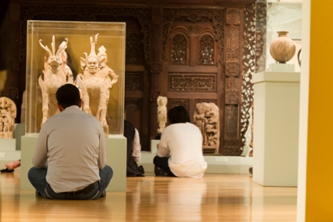 student sitting on floor of museum in Asian galleries looking at sculptures of anamorphic deities that are part dog and part human made of stone